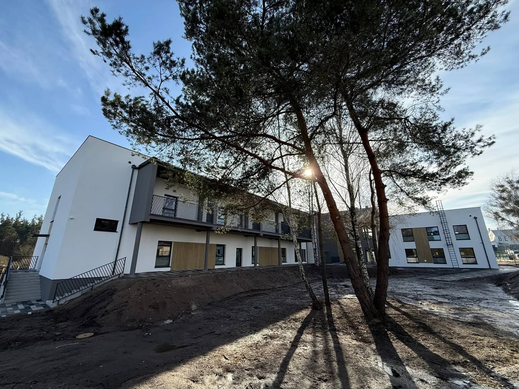 Zakład opiekuńczo-pielęgnacyjny po rozbudowie — widok od strony drzew i terenu zewnętrznego